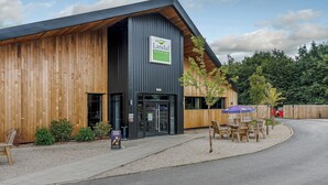 A building with a sign reading 'Landal Woodland Lake,' a wooden exterior, and outdoor seating with a table and chairs. - Pine Lodge Spa Pet (Thirsk)
