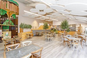 Ein geräumiges Restaurant mit runden Tischen und Stühlen, einer Holztheke und einem Spielbereich für Kinder.