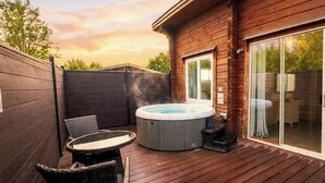 A wooden deck with a hot tub, wicker furniture, and a sliding glass door leading to a room. - Pine Lodge Spa Pet (Thirsk)