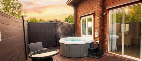 A wooden deck with a hot tub, wicker furniture, and a sliding glass door leading to a room.