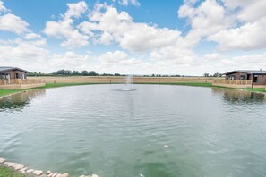 A tranquil outdoor pool with a fountain, surrounded by wooden decks and two buildings. - Pine Lodge Spa Pet (Thirsk)