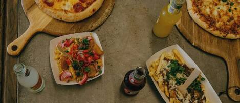A table with three pizzas, a dish with fries, and two bottles of sauce.