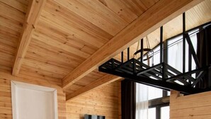 Ein modernes Interieur mit Holzbalkendecke, einem Esstisch mit Stühlen, einer Couch und einem an der Wand montierten Fernseher.
