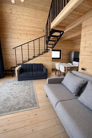 Un interior de madera con una escalera, dos sofás, una mesa de comedor y un televisor.
