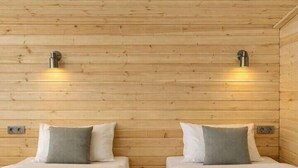 Ein Zimmer mit zwei Betten, jeweils mit grauer Bettdecke und Kissen, sowie einem gefalteten Handtuch auf dem Bett.