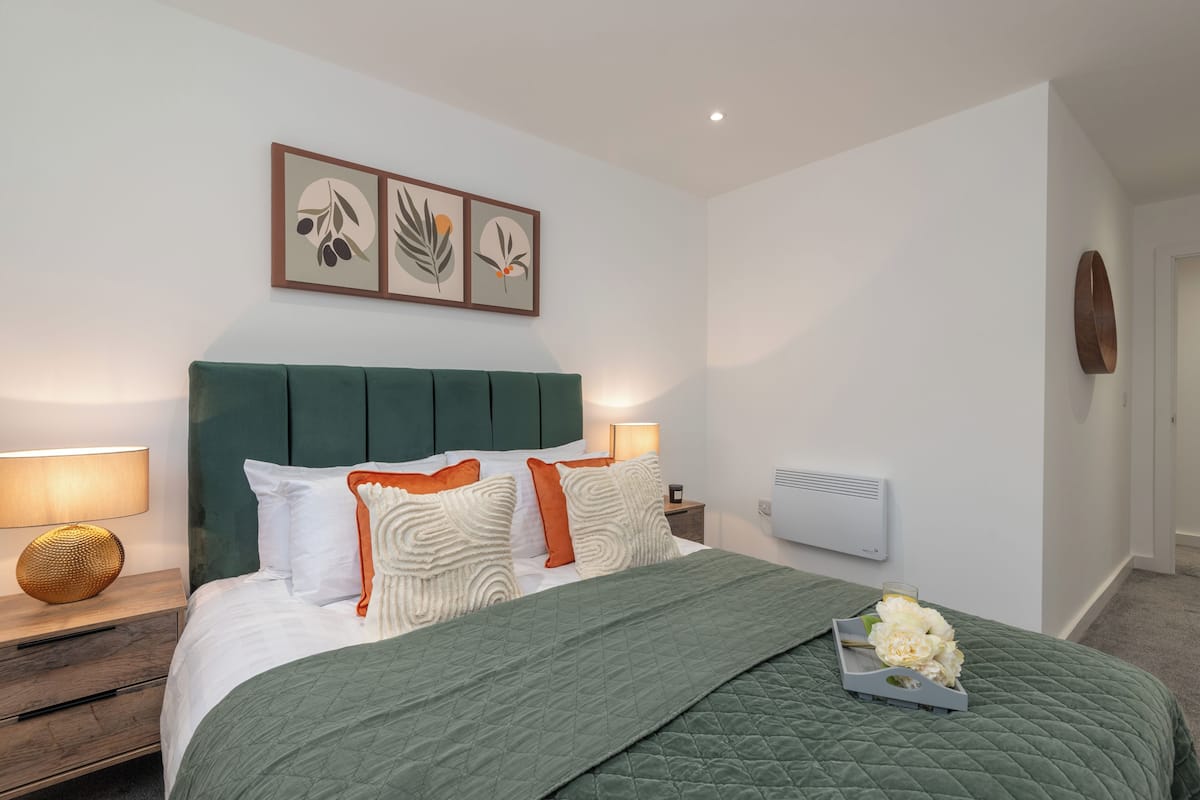 Un dormitorio ordenado con cama, mesitas de noche, aire acondicionado de pared y cuadros enmarcados.