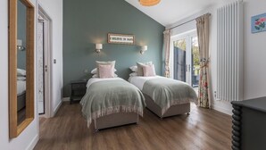 A bedroom with two beds, a wooden floor, a green accent wall, and a view of the outdoors.