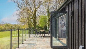 An outdoor patio with stone flooring, a glass door leading to a building, and a table with chairs.