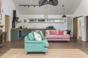 Une cuisine moderne dotée d’un îlot central intégré, un coin repas avec un canapé rose et un fauteuil vert.