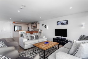 A modern living room with a sofa, coffee table, and a flat-screen TV. - Ohope Beach Resort (Ōhope)