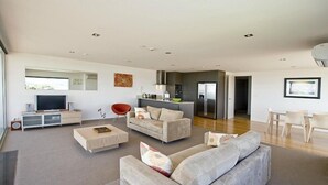 A modern living room with a flat-screen TV, a red chair, a grey sofa, and a kitchen area with a fridge and stove.