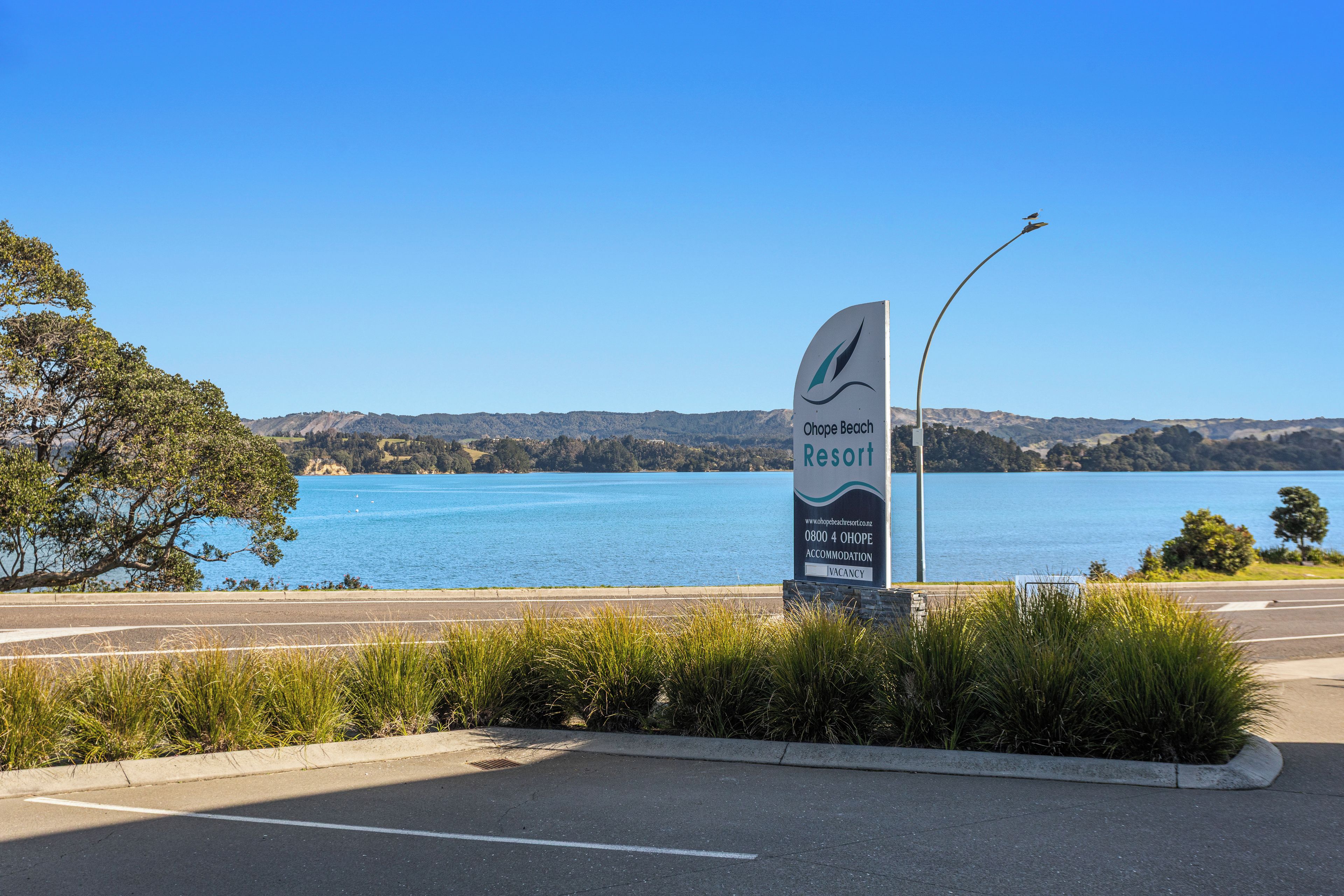 A sign for Ohpe Beach Resort with a view of a lake and hills in the background.