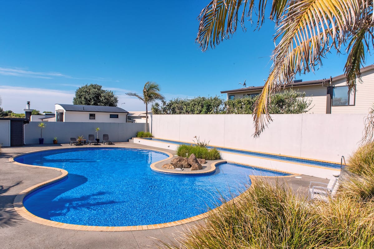 A swimming pool with a curved edge, surrounded by a white wall, with a clear blue sky above.