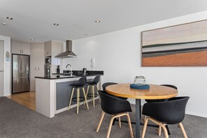A modern kitchen with a central island, bar stools, and a dining table with chairs. - Ohope Beach Resort (Ōhope)