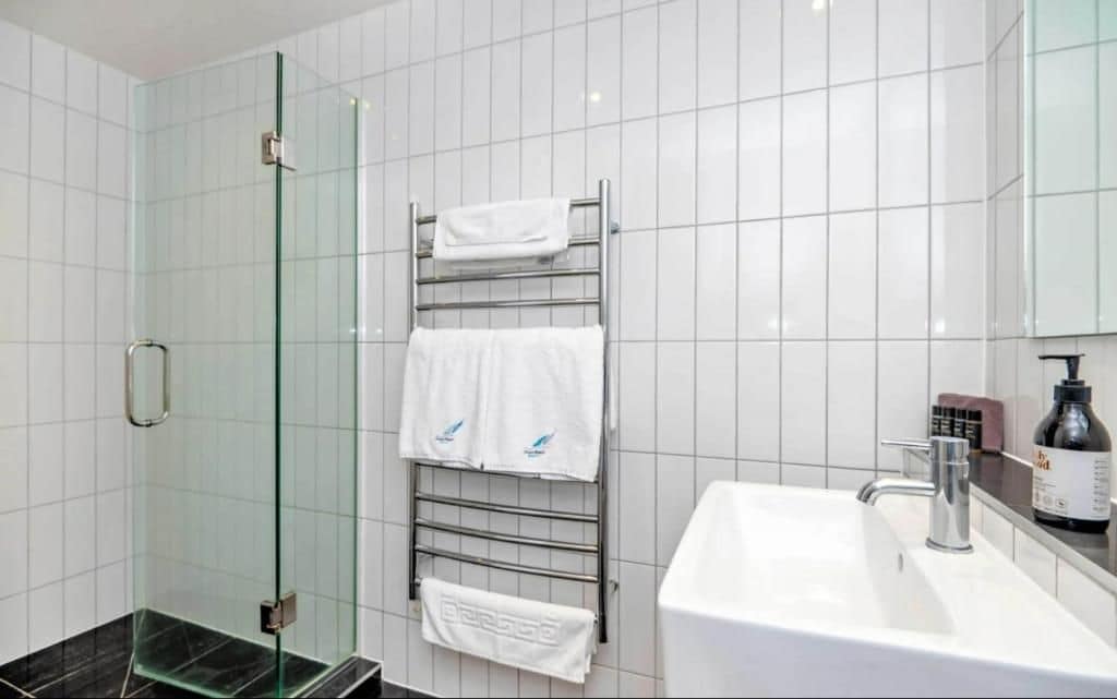 A modern bathroom with a glass shower enclosure, a white sink, and a towel rack with multiple towels.