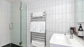 A modern bathroom with a glass shower enclosure, a white sink, and a towel rack with multiple towels.