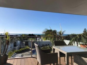 Ein Balkon mit Korbmöbeln, einem Glastisch und Blick auf das Meer.