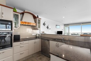 A modern kitchen with a built-in oven, a dishwasher, and a large island with a sink. - Ohope Beach Resort (Ōhope)