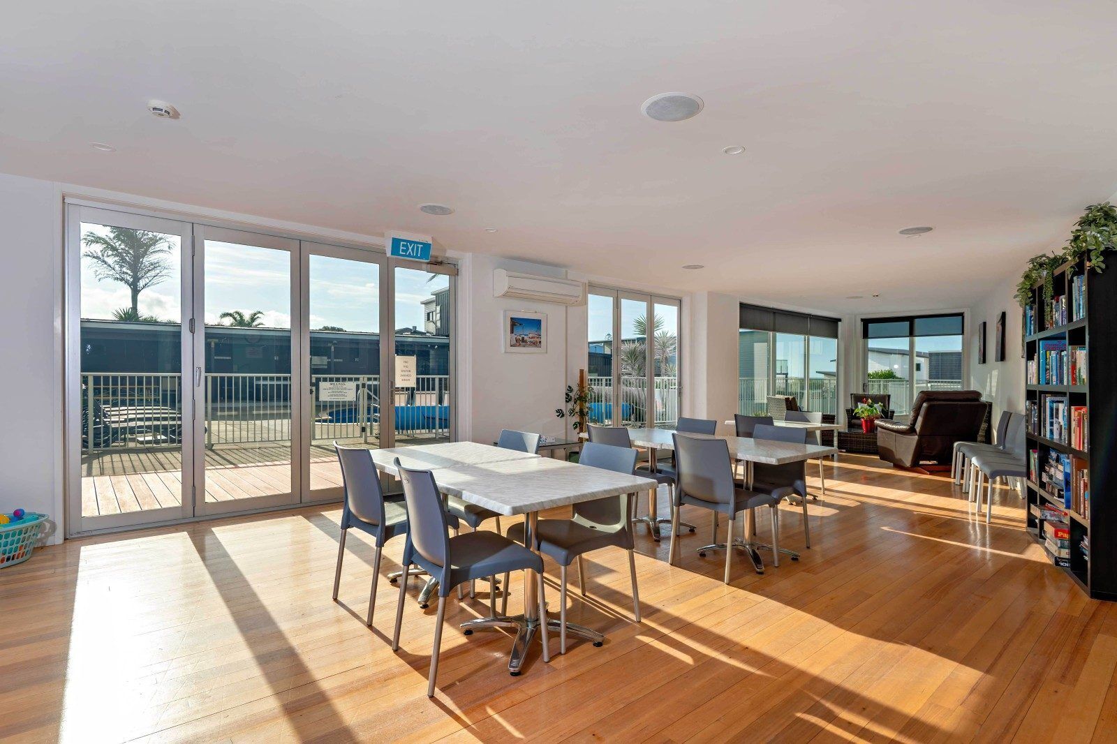 A spacious room with a large table and chairs, a bookshelf, and a balcony with a view.