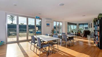 A spacious room with a large table and chairs, a bookshelf, and a balcony with a view.