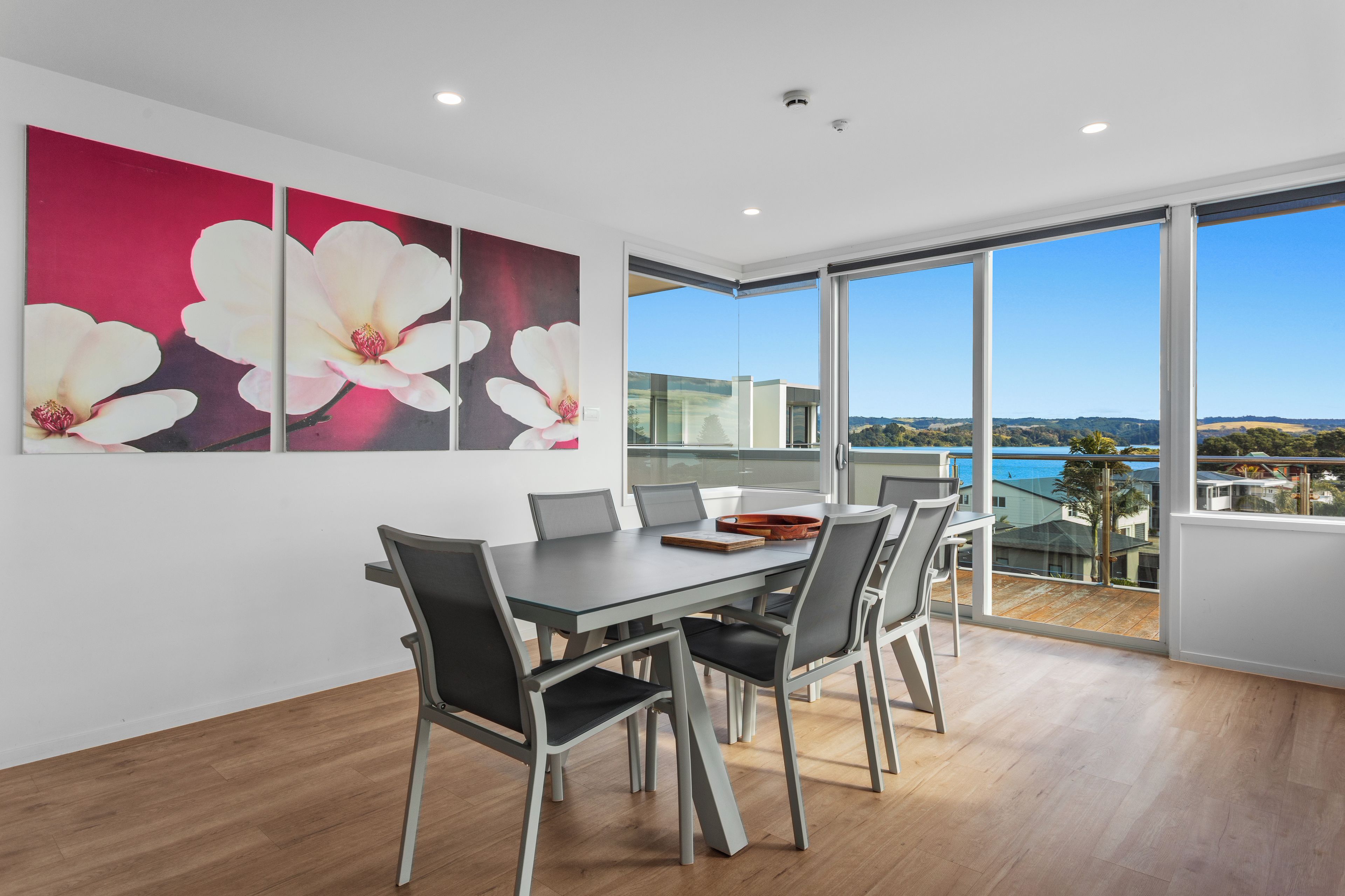 A dining area with a table and chairs, large windows with a view, and wall art.