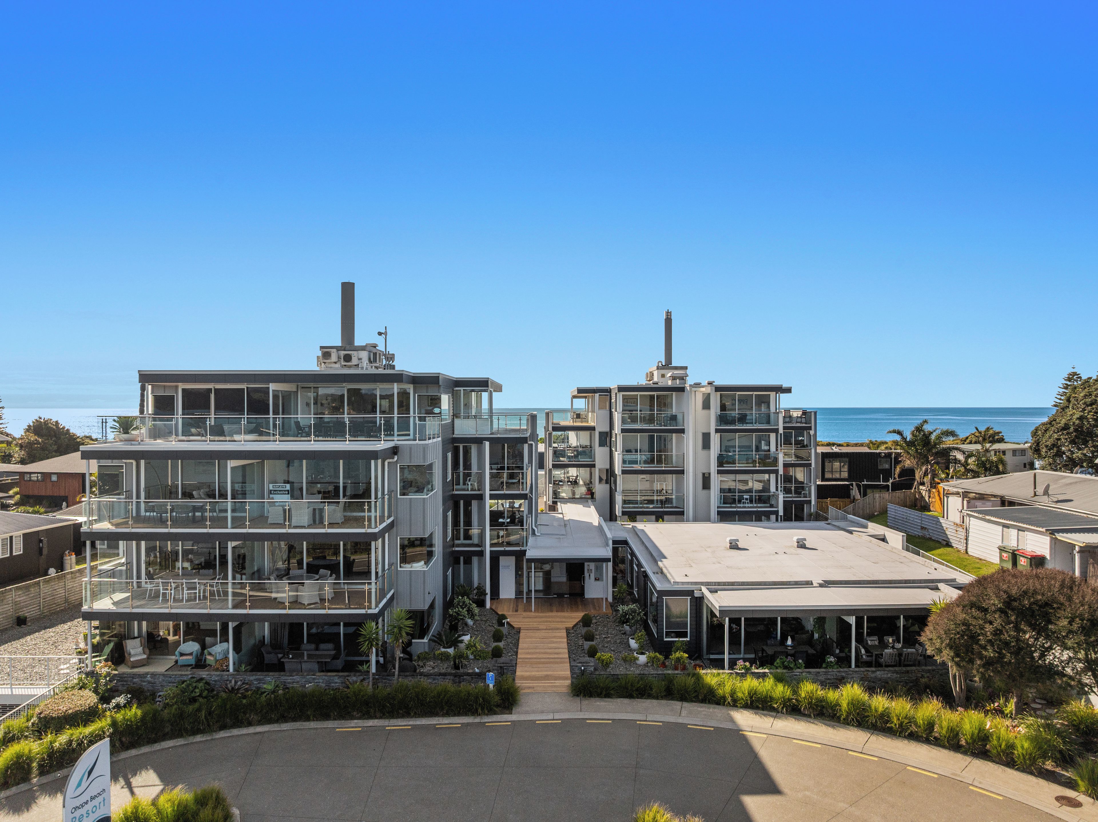 A modern hotel with multiple floors, large windows, and a view of the ocean.