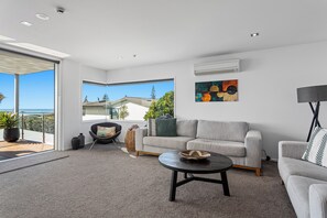 A modern living room with a grey sofa, a round coffee table, and a view of the sea through large windows. - Ohope Beach Resort (Ōhope)