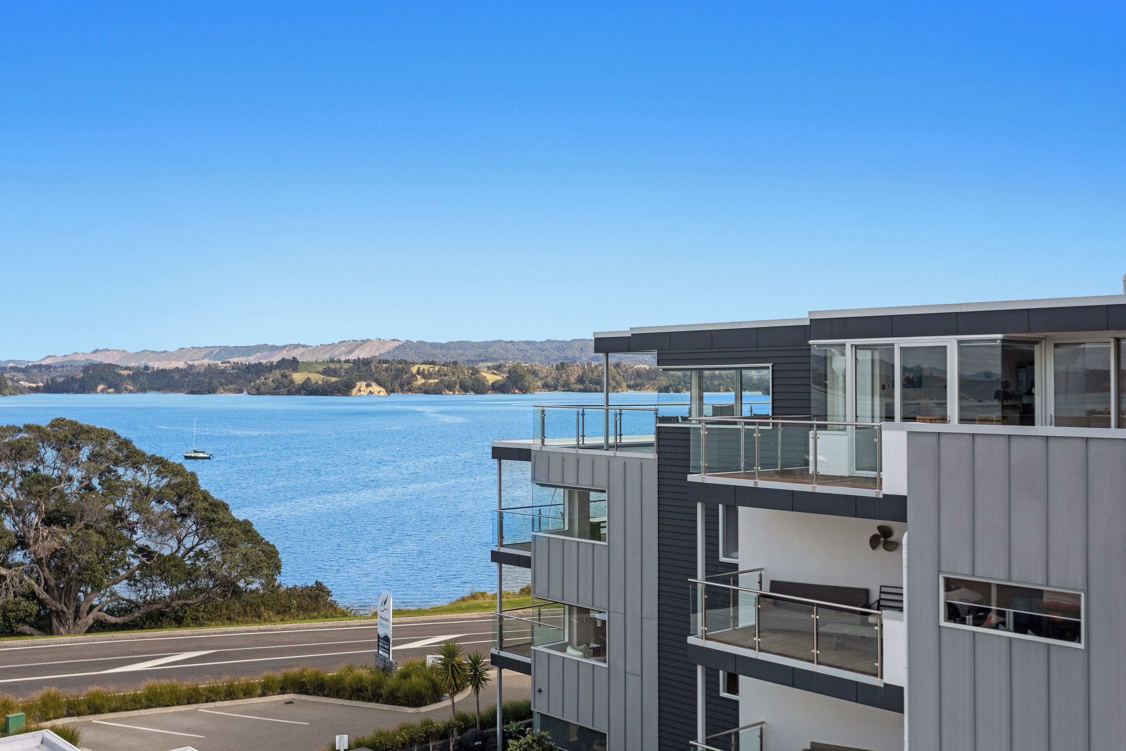 A modern multi-story building with balconies overlooking a body of water and distant hills.