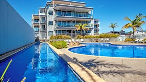 A modern hotel with a pool, multiple balconies, and palm trees.
