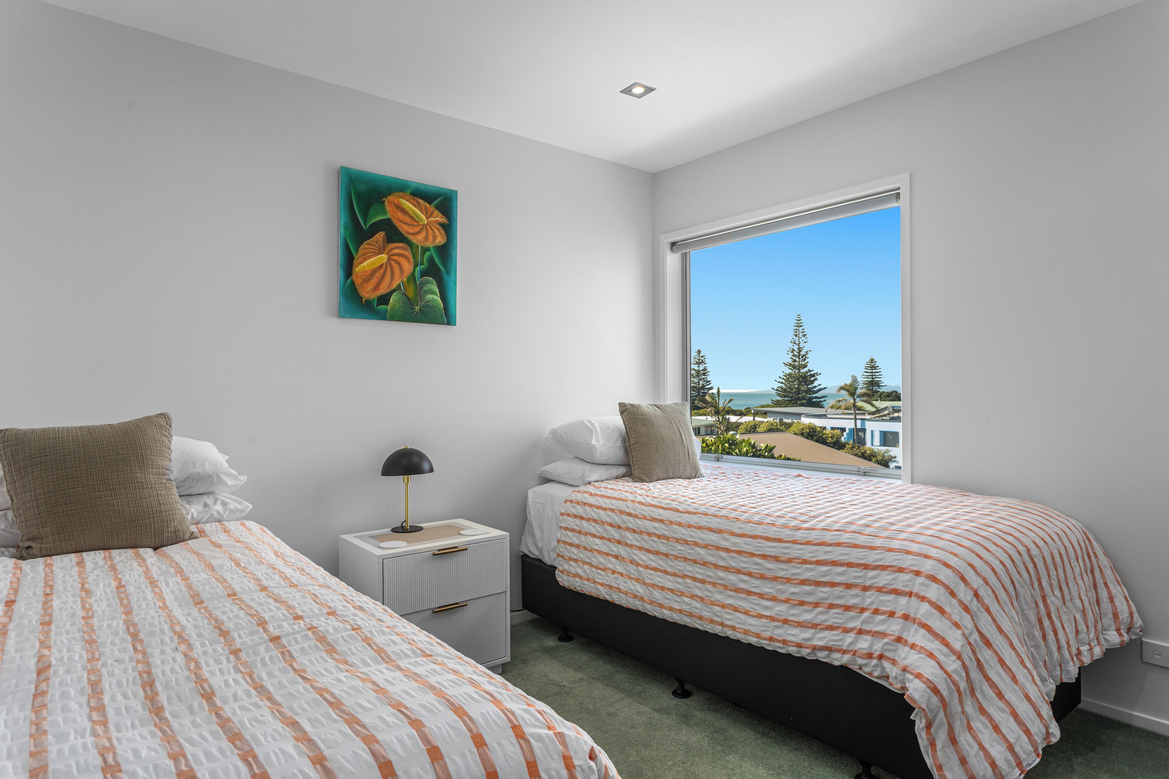 A bedroom with two beds, a nightstand, a lamp, and a painting on the wall.