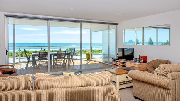 A modern living room with a large sliding glass door leading to a balcony with a view of the ocean.
