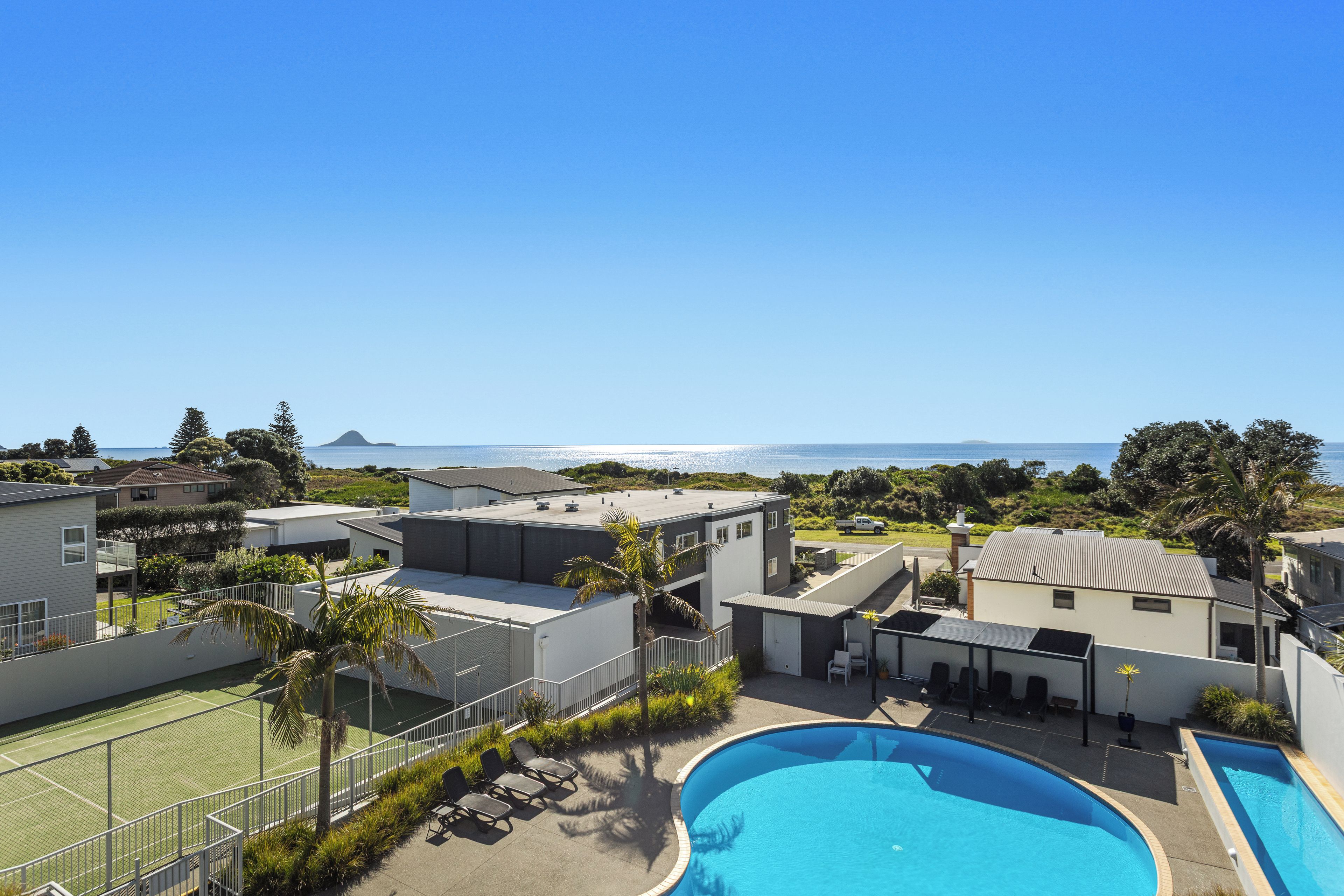 Un quartier résidentiel doté d’une piscine, d’un court de tennis et de maisons offrant une vue sur la mer.