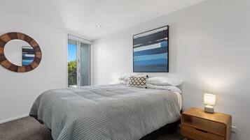 A bedroom with a bed, a bedside table, a nightstand, a wall-mounted mirror, and a painting.