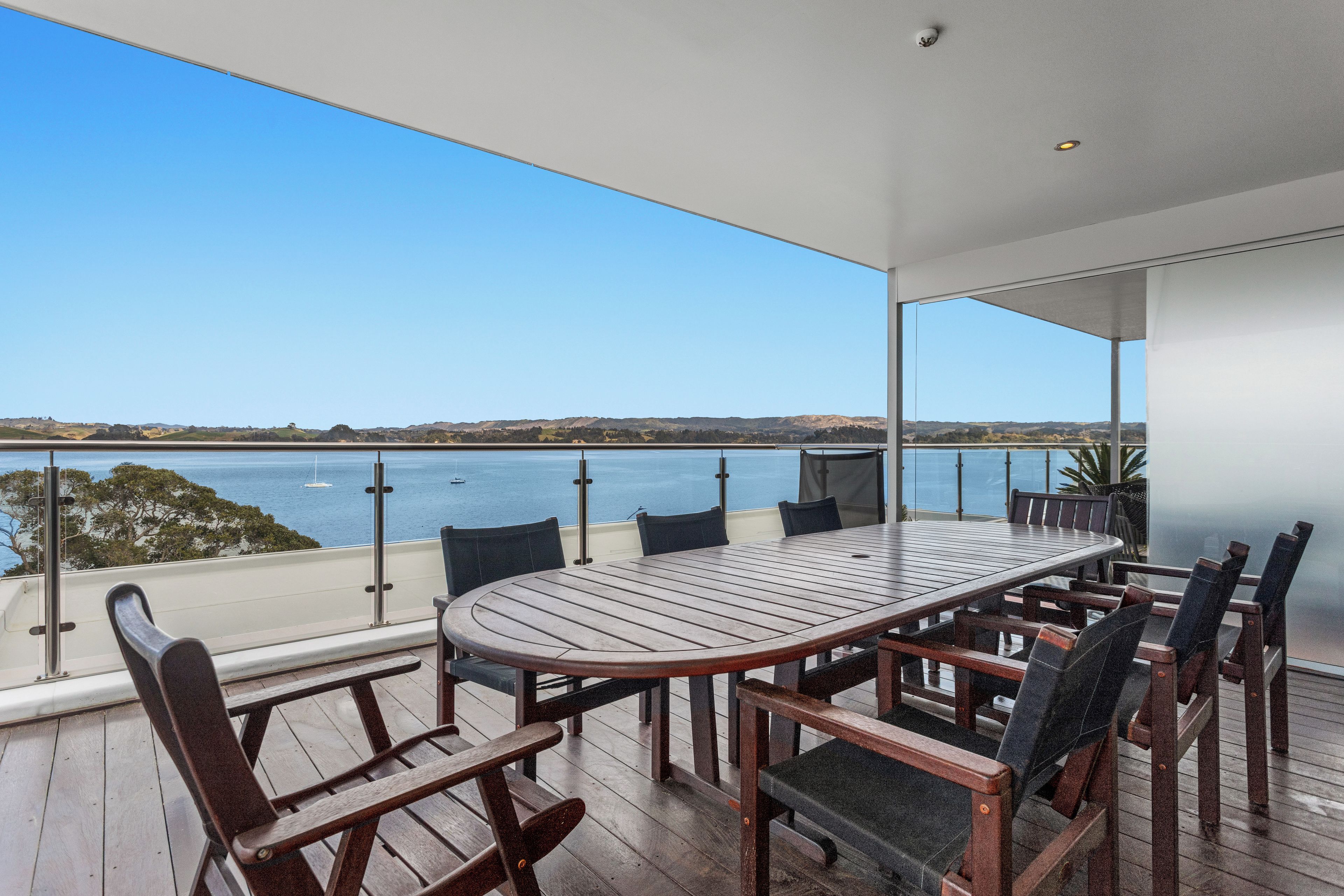 A terrace with a view of the sea, a round table, and chairs.