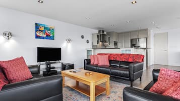 A modern living room with a flat-screen TV, leather sofas, a wooden coffee table, and a colorful rug.