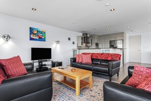A modern living room with a flat-screen TV, leather sofas, a wooden coffee table, and a colorful rug.