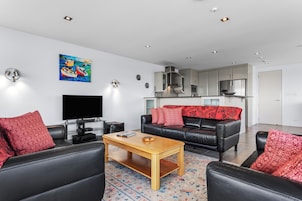 A modern living room with a flat-screen TV, leather sofas, a wooden coffee table, and a colorful rug.