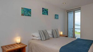 A bedroom with a bed, pillows, a bedside table with a lamp, and three paintings on the wall.