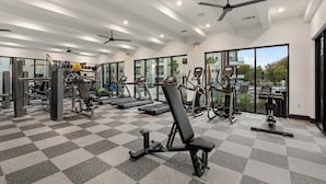 Et fitnesscenter med forskellig træningsudstyr, store vinduer og loftvifte.