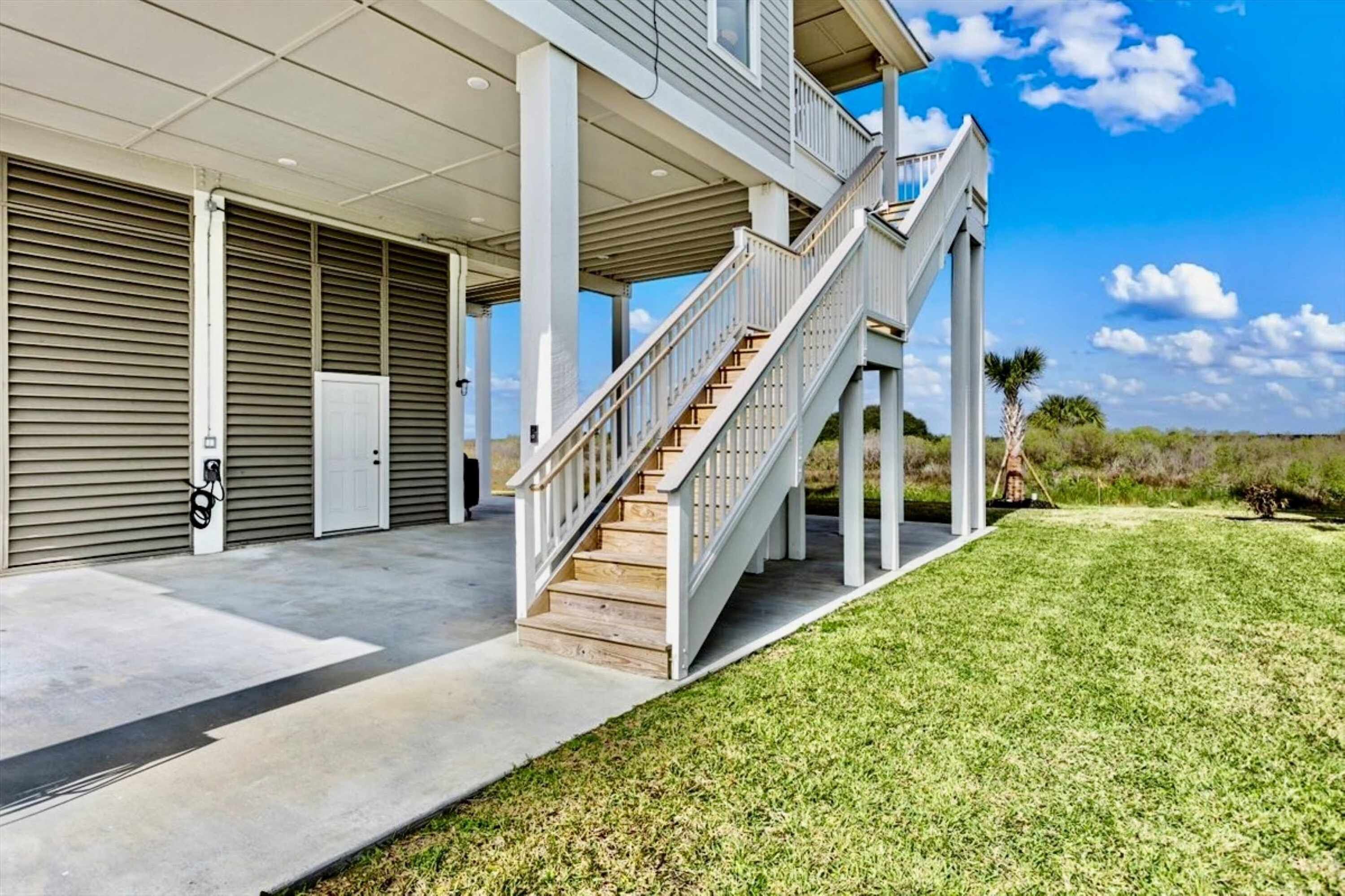 A two-story building with a covered outdoor area, a staircase, and a grassy lawn.