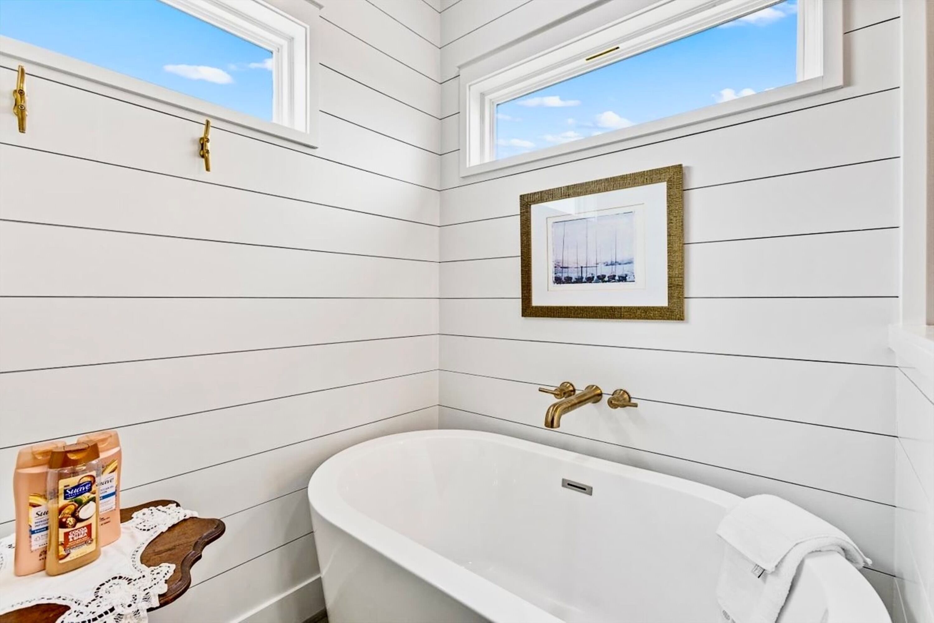 Un baño con una bañera independiente, un cuadro enmarcado en la pared y una ventana con vistas al cielo.