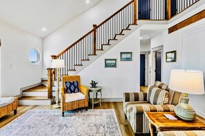 A spacious living area with a staircase, a wicker chair, a striped sofa, and a lamp. - Spoonbill at West Bay (Galveston)