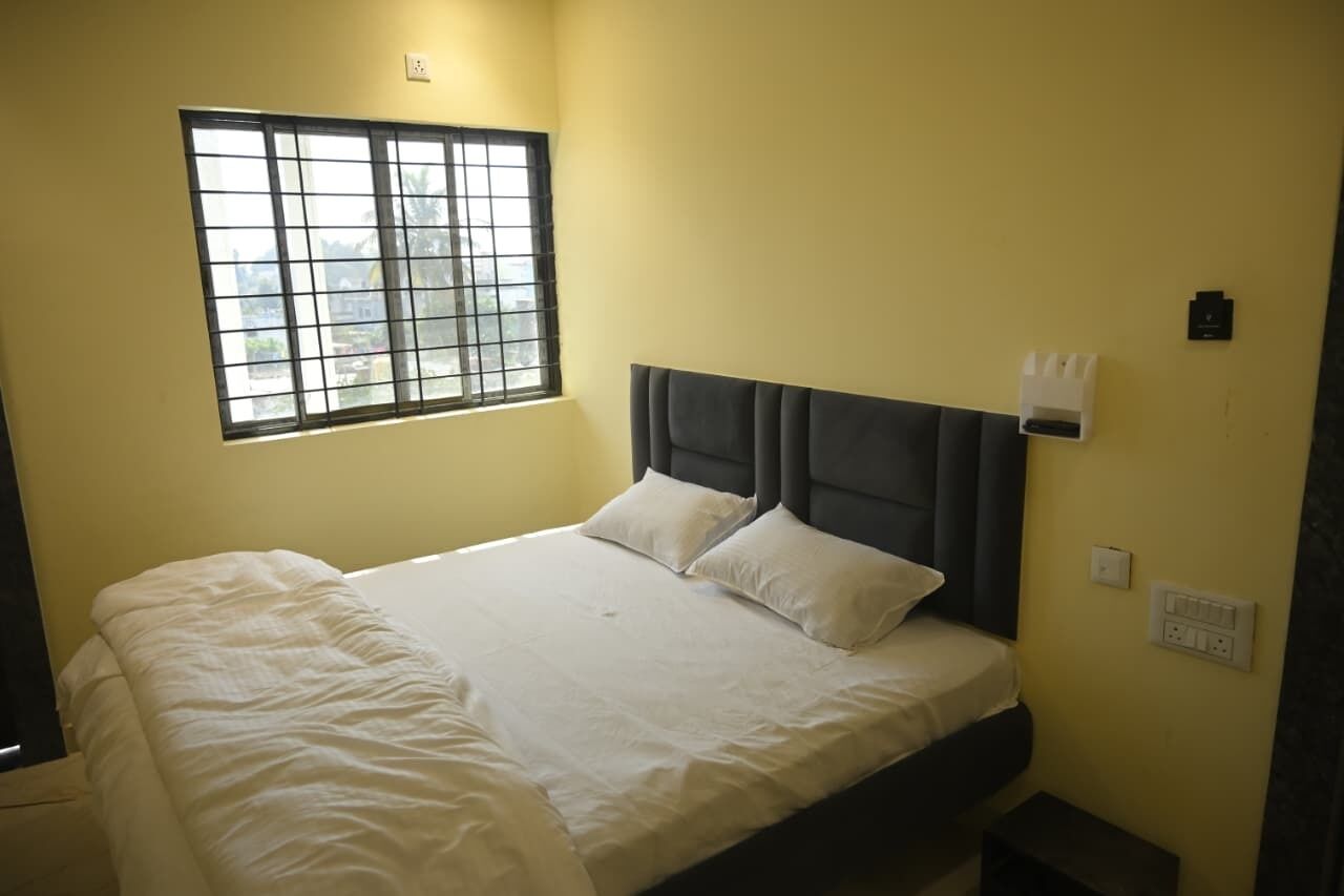 A single bed with a headboard, a window with metal bars, and a wall-mounted light switch.