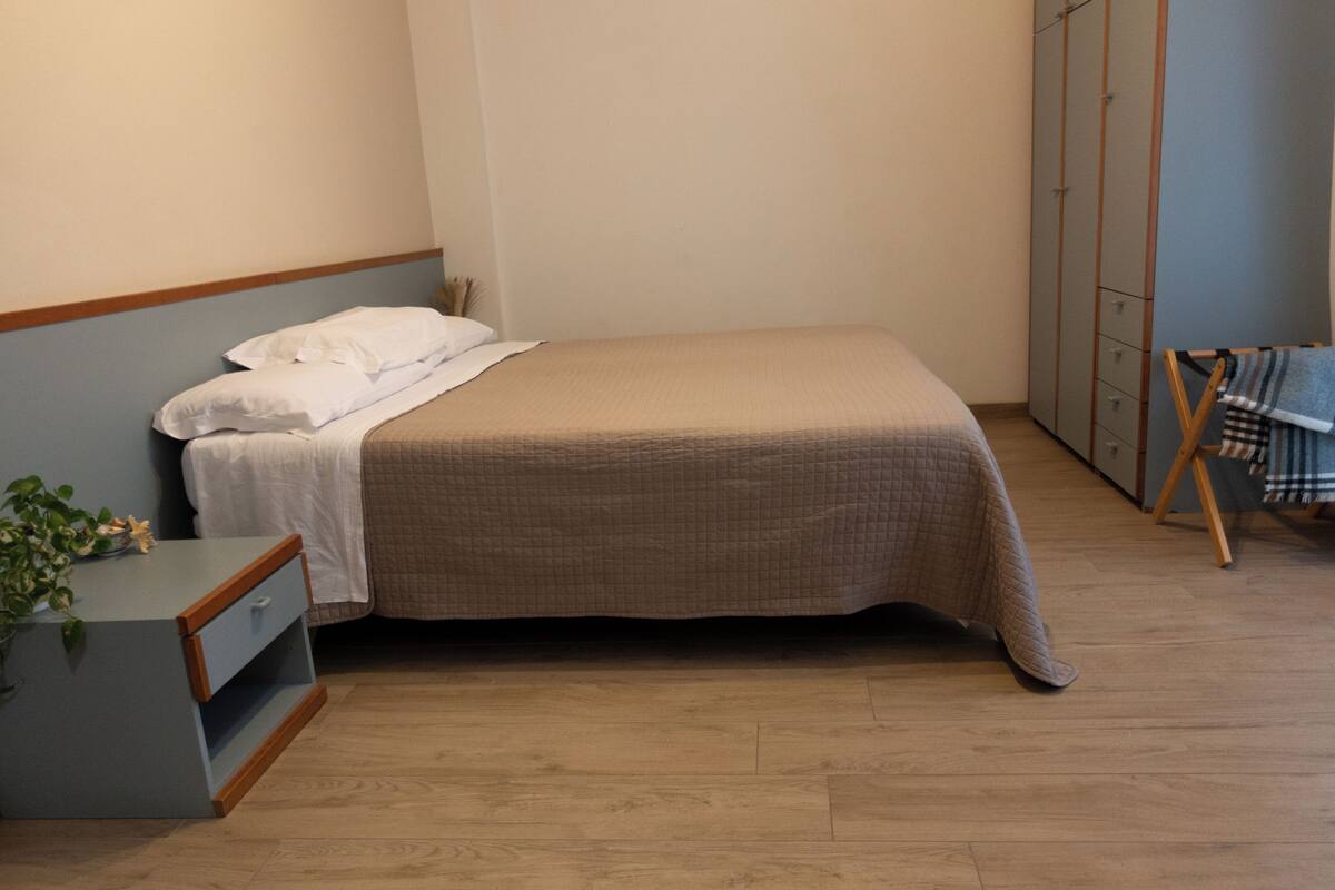 Una cama individual con cubrecama acolchado, una mesita de noche con una planta y un armario con varias puertas.