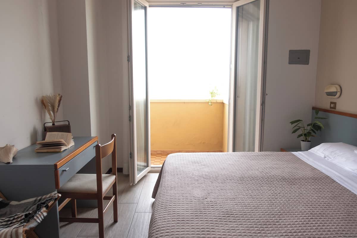 Un dormitorio con cama, escritorio, silla, ventana y una planta en maceta.