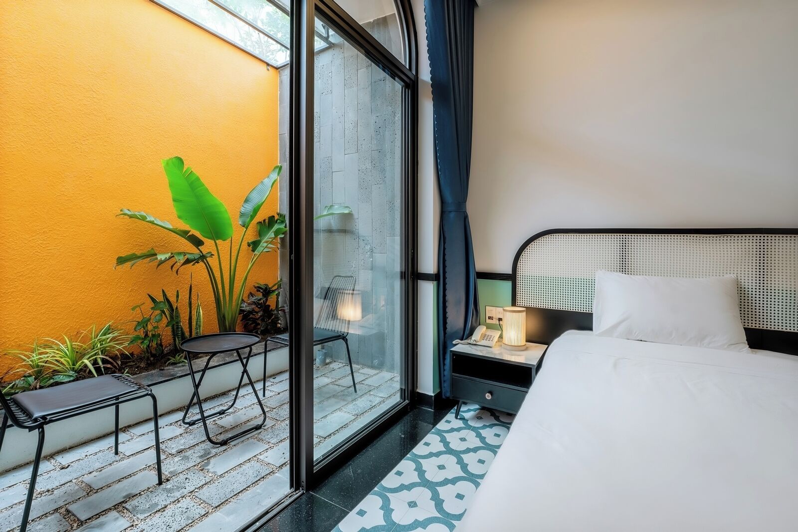 A hotel room with a bed, a nightstand, a lamp, a chair, and a small table.
