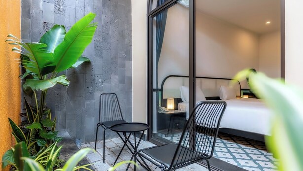 A hotel room with a bed, a nightstand, a lamp, a chair, and a small table. - Hoi An Ivy Hotel (Da Nang)