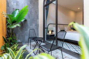 A hotel room with a bed, a nightstand, a lamp, a chair, and a small table. - Hoi An Ivy Hotel (Da Nang)