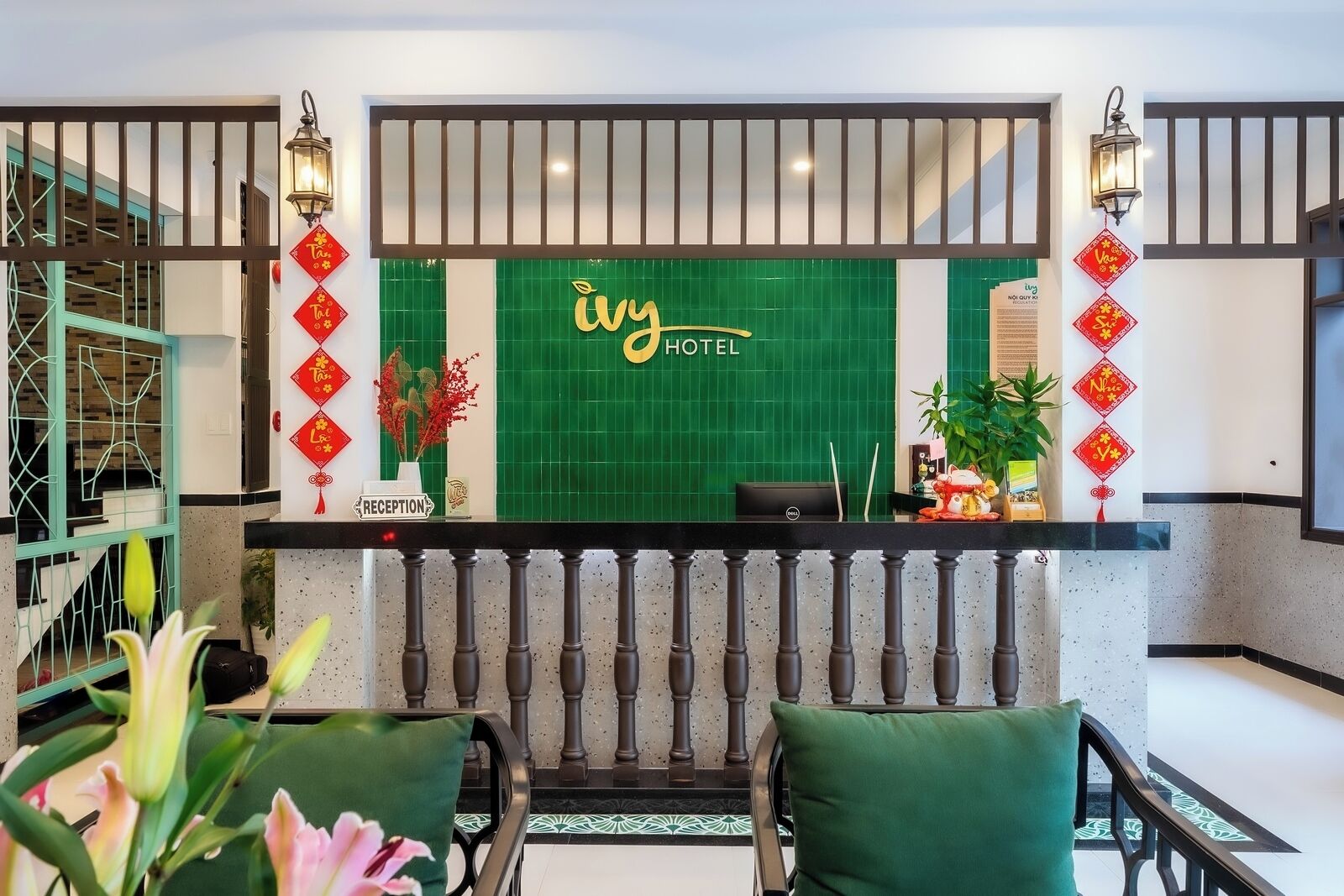 Zona de recepció d'hotel amb una paret de rajoles verdes, un taulell de recepció i làmpades decoratives vermelles.