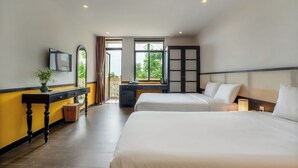 A hotel room with two beds, a desk, a TV, and a view of greenery outside. - Hoi An Ivy Hotel (Da Nang)